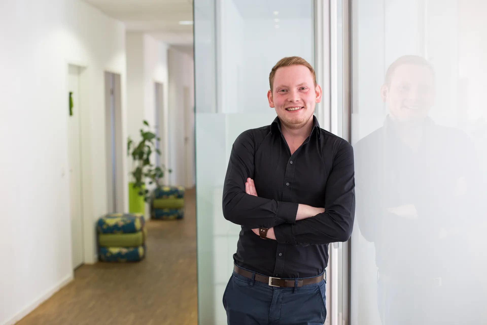 Maximilian Eckel, Gründer von BespokeCode, angelehnt an eine Glasfront in einem hellen Raum.